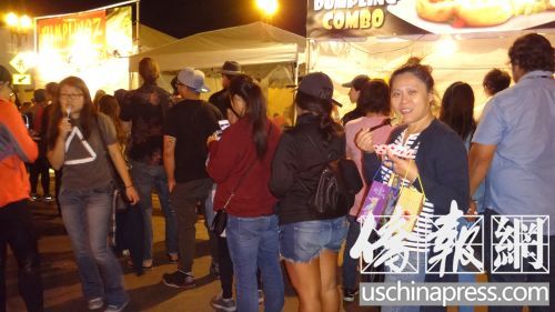 圣蓋博教會路餃子攤亭一個挨一個，每個攤亭前都大排長龍，圣蓋博居民鄧曉玲女士(右二)一邊吃餃子一邊排隊。(僑報記者高睿攝)