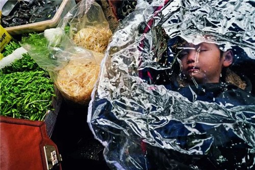 在紐約唐人街，你能買到最新鮮的魚、肉和蔬菜，也能吃到最正宗的中國(guó)菜，圖中，菜市場(chǎng)的孩子在菜攤旁熟睡。