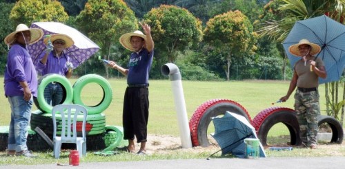 大家戴著草帽、撐著傘，在烈日下美化校園。（馬來西亞《星洲日?qǐng)?bào)》）