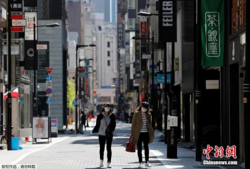 日本東京，戴口罩的女士走過空無一人的購物區(qū)。